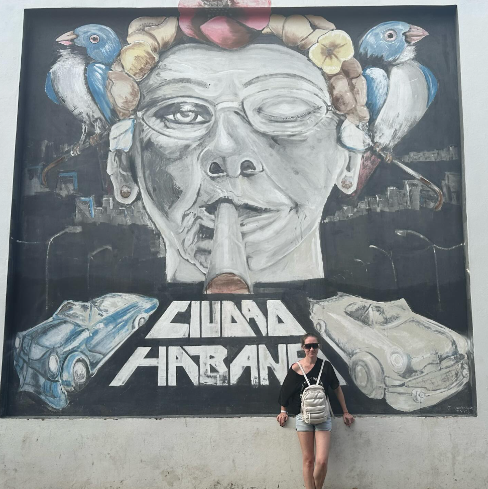Мария у мурала «Ciudad Habana» с изображением курильщика и попугаев