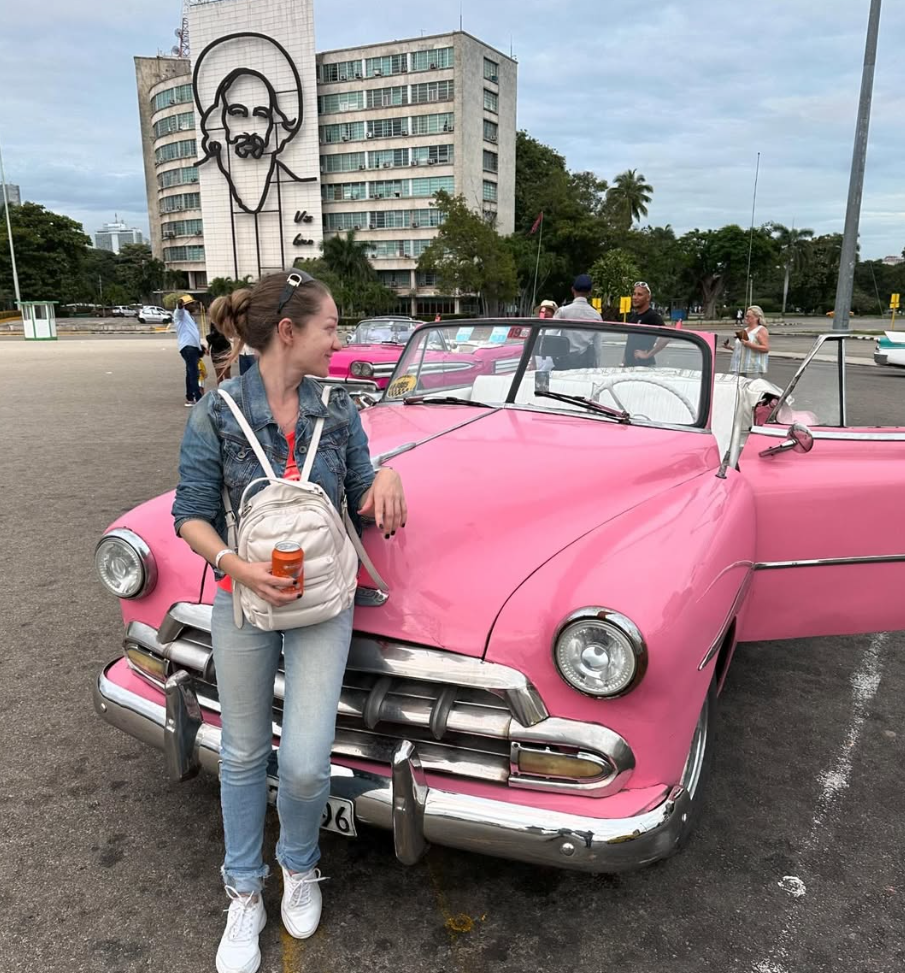 Мария у розового Chevrolet на Площади Революции в Гаване, фоном — портрет Че Гевары