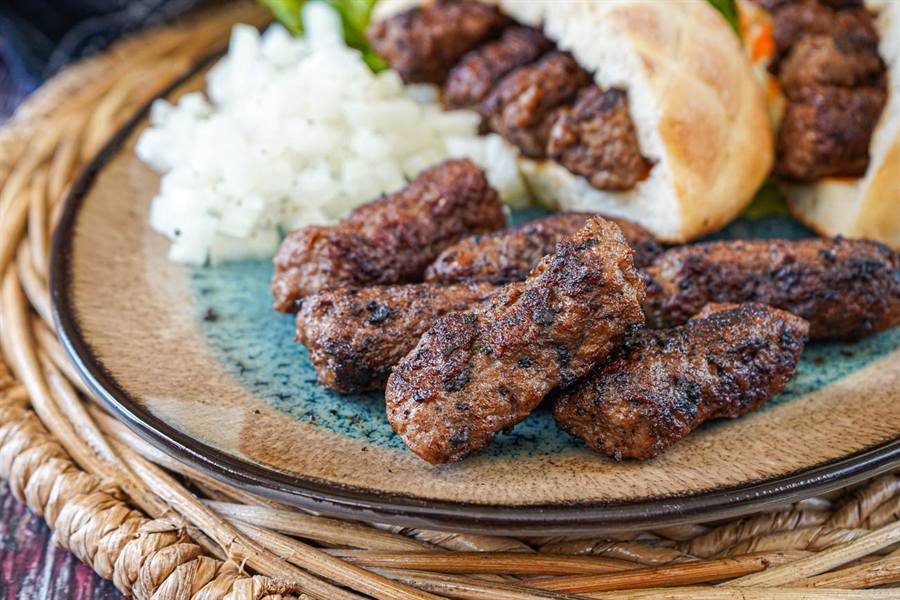 A plate of grilled Balkan ćevapi served with chopped onions and flatbread